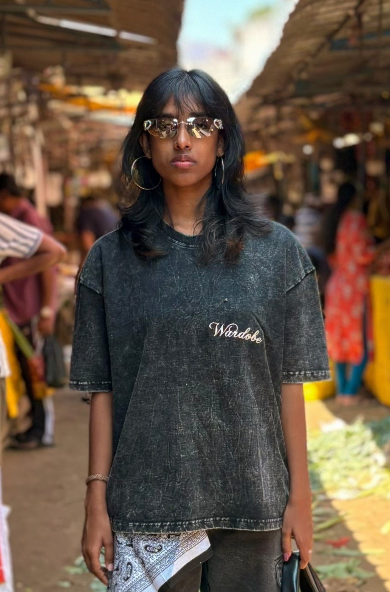Person wearing a black t-shirt with 'Wardrobe' text in an outdoor market setting